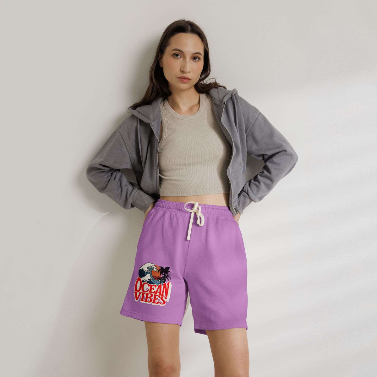 A woman stands against a light gray wall wearing purple drawstring shorts with a colorful 'Ocean Vibes' graphic on the left leg, a beige crop top, and a gray zip-up hoodie. Unique Lightweight Fleece Sweat Shorts in Ocean Vibes Graphic Shop Lightweight Fleece Sweat Shorts in Ocean Vibes for breezy comfort, relaxed style, and an easygoing summer-ready look all day. Refresh your casual rotation with Lightweight Fleece Sweat Shorts in Ocean Vibes—soft, versatile, and ready for sunny days by the shore.