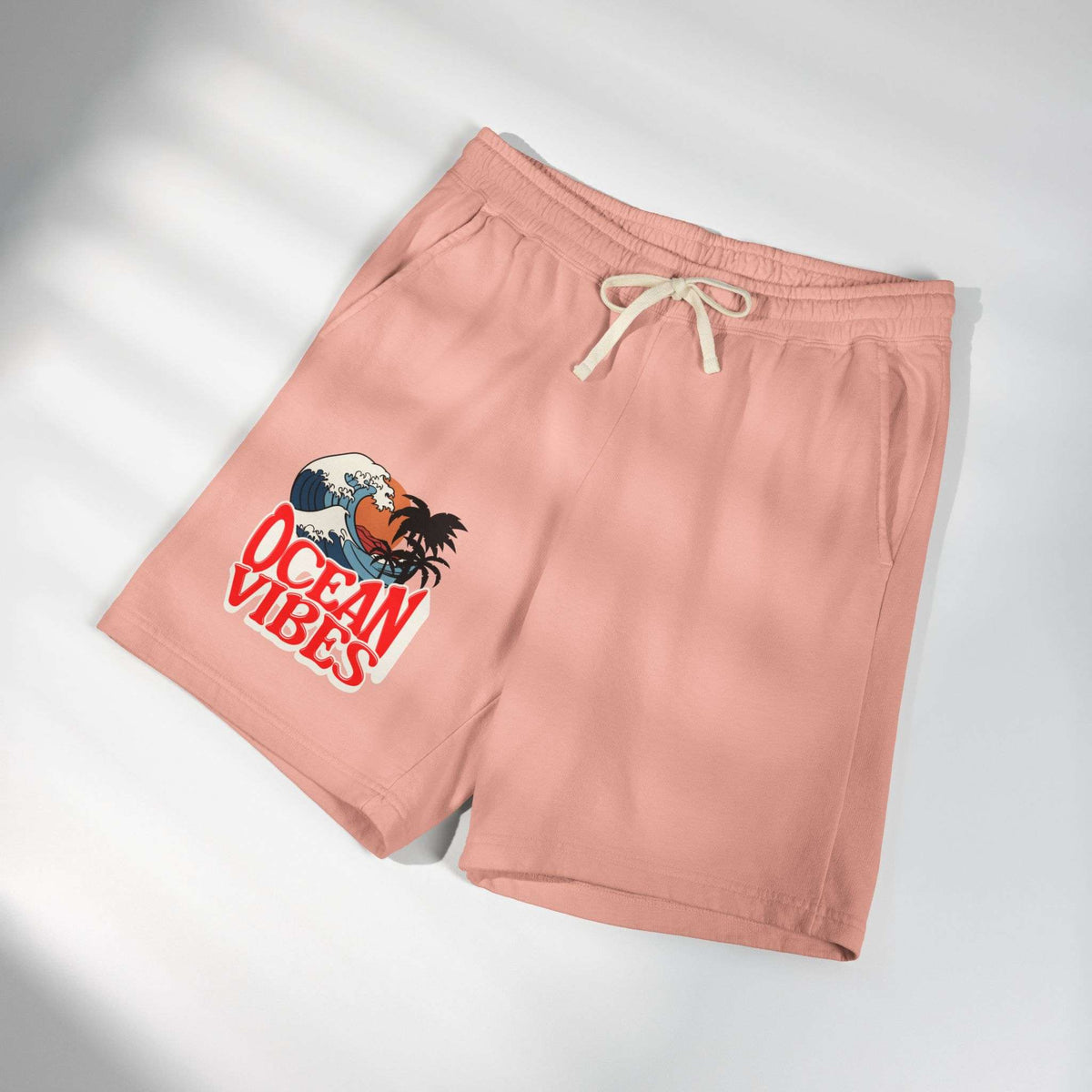 A pair of dusty pink athletic shorts with a cream drawstring, featuring a graphic print of a Hawaiian character in a wave with the text 'OCEAN VIBES' on the left leg, displayed on a light gray background with soft diagonal shadows. Unique Lightweight Fleece Sweat Shorts in Ocean Vibes Graphic Shop Lightweight Fleece Sweat Shorts in Ocean Vibes for breezy comfort, relaxed style, and an easygoing summer-ready look all day. Refresh your casual rotation with Lightweight Fleece Sweat Shorts in Ocean Vibes.