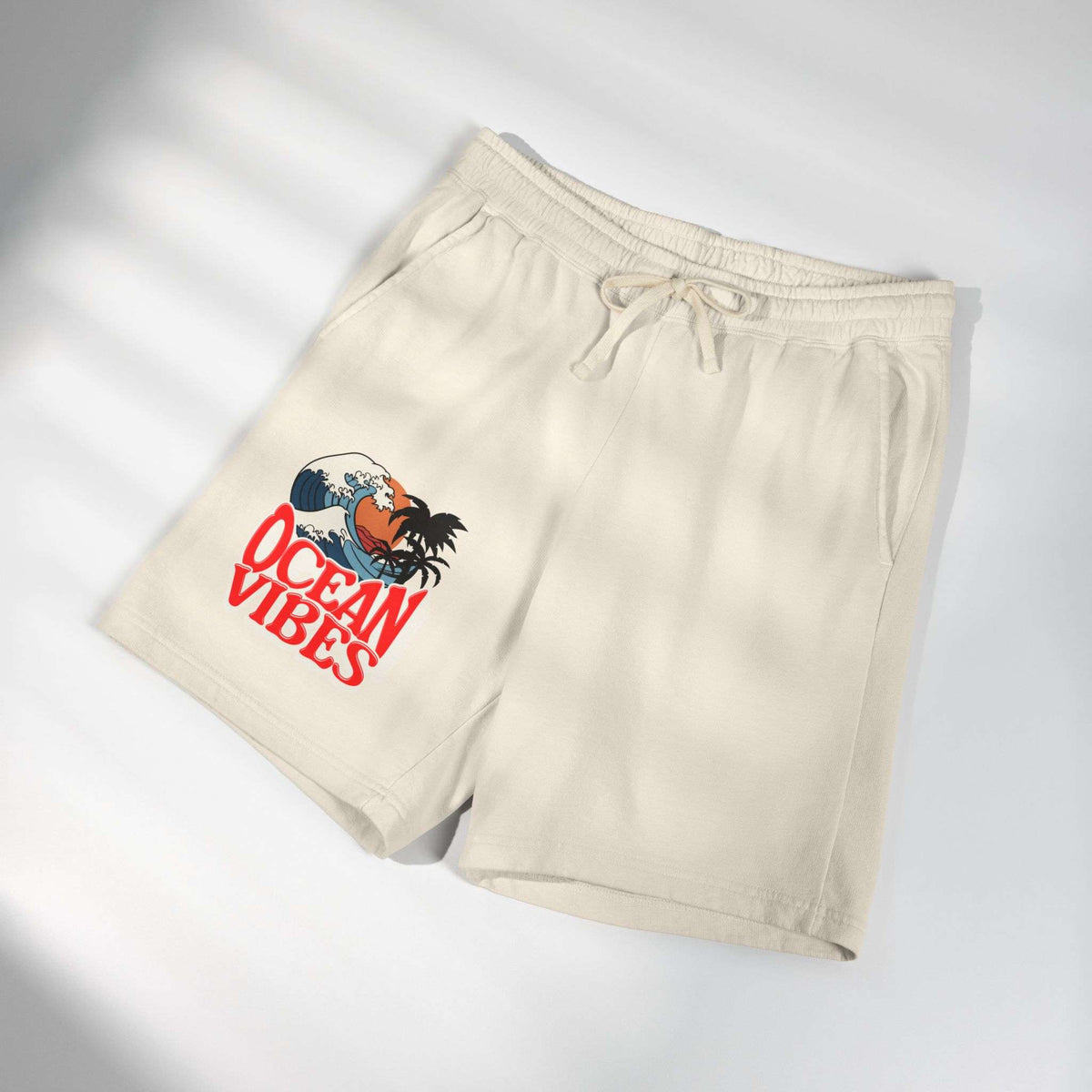 Beige drawstring shorts with a graphic print on the left leg featuring a rooster and the text 'OCEAN VIBES' in red, shown on a white background with soft diagonal shadows.