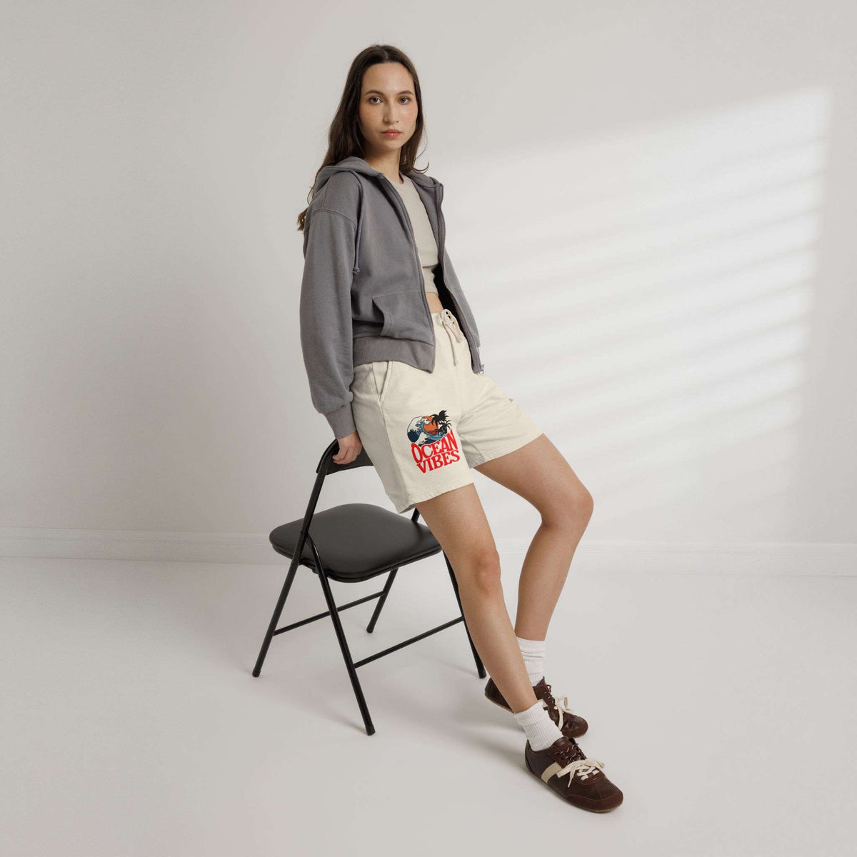Woman wearing a gray hoodie and beige shorts with floral patterns, standing next to a black chair on a plain background. Unique Lightweight Fleece Sweat Shorts in Ocean Vibes Graphic Shop Lightweight Fleece Sweat Shorts in Ocean Vibes for breezy comfort, relaxed style, and an easygoing summer-ready look all day. Refresh your casual rotation with Lightweight Fleece Sweat Shorts in Ocean Vibes—soft, versatile, and ready for sunny days by the shore. Buy Lightweight Fleece Sweat Shorts in Ocean Vibes.