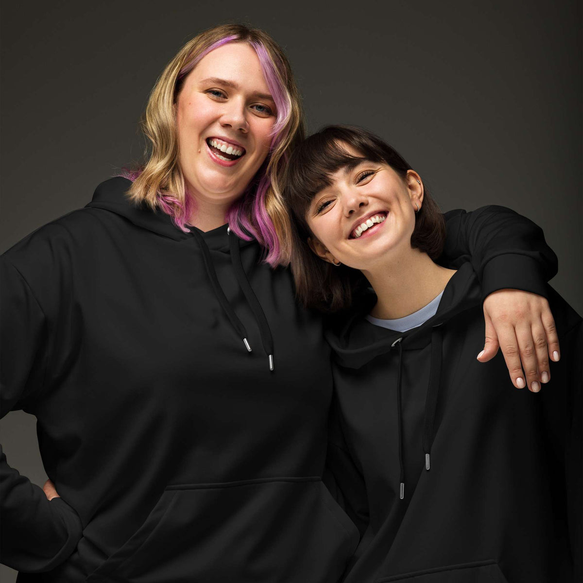 Two women smiling and posing together while wearing matching black hoodies against a dark gray studio background. Comfortable Minimalist Bold Plain Midnight Black Hoodie for Relaxed Wear