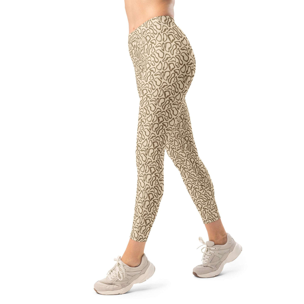 A person modeling high-waisted leggings with an all-over abstract line pattern in beige and brown, paired with light beige sneakers, shown against a plain white background.