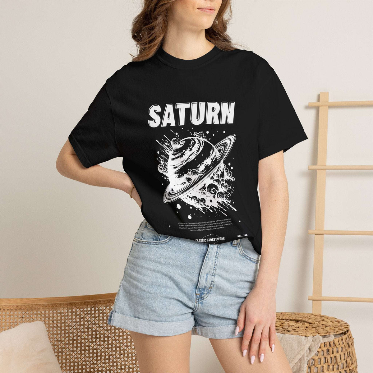 A woman wearing a black graphic t-shirt with a green and beige 'RUIN' character print, paired with light blue denim shorts, standing in a brightly lit indoor setting.