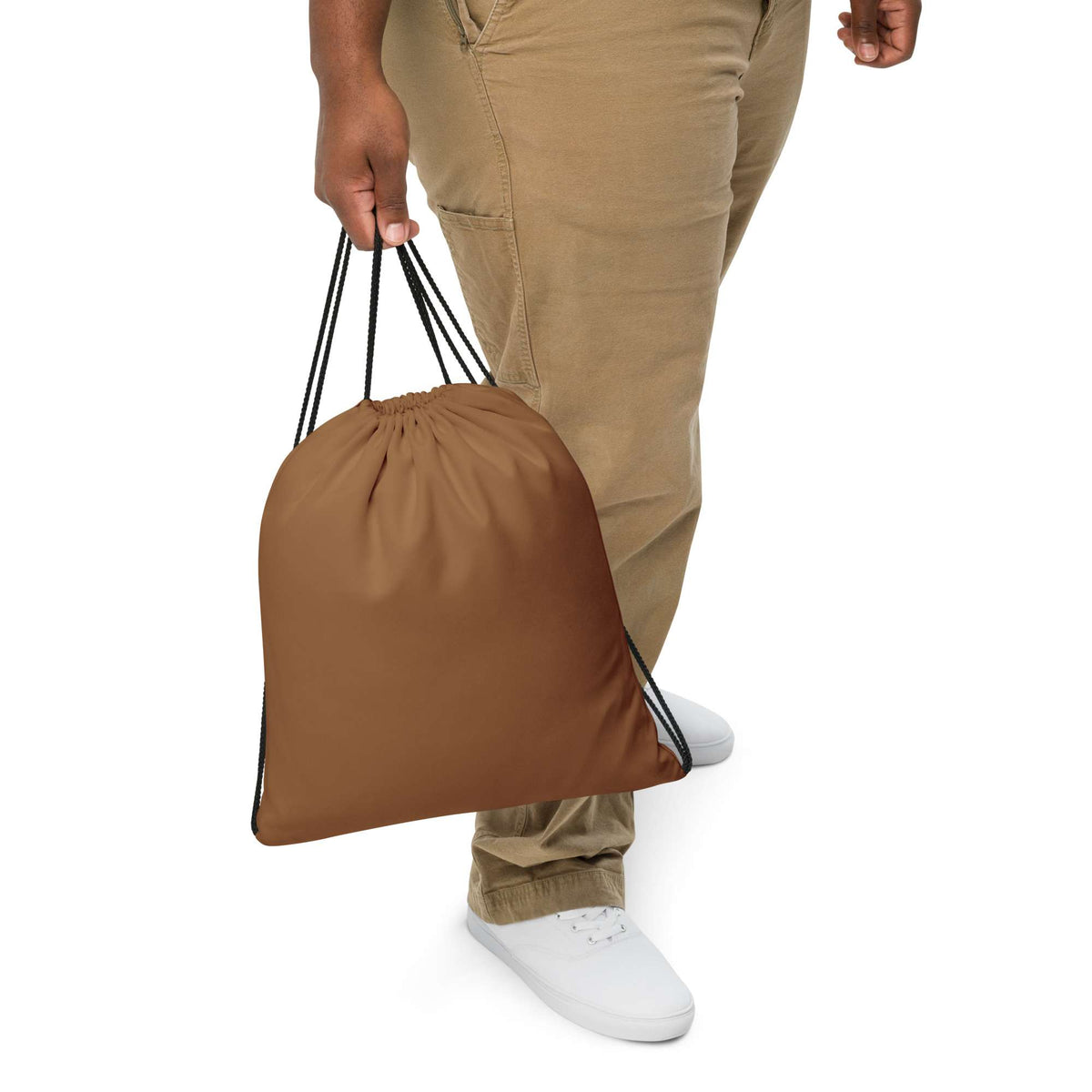 A person wearing khaki pants and white sneakers holds a plain brown drawstring bag against a white background. Durable Bold Minimalist Solid Natural Wood Drawstring Bag