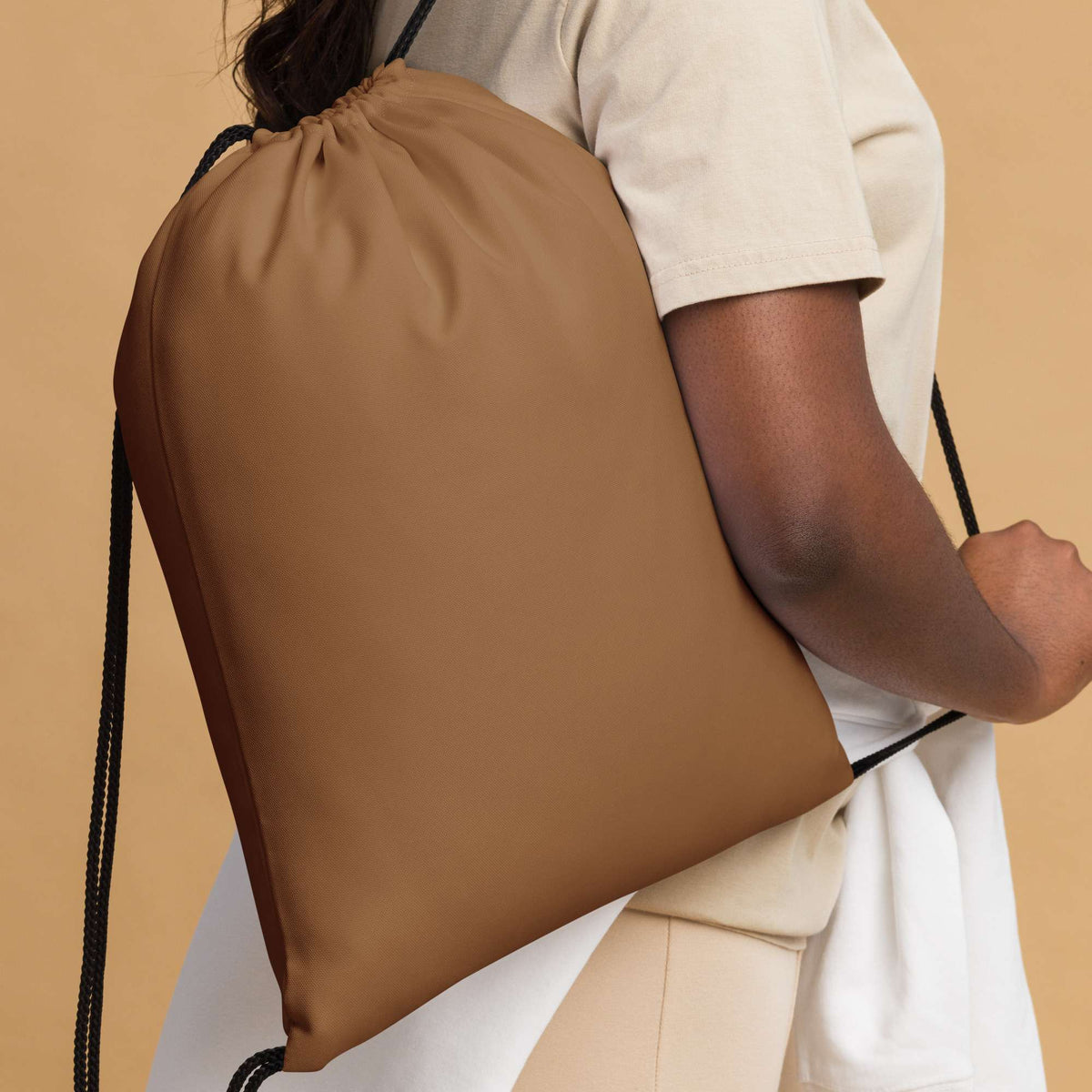 A person wearing a cream-colored outfit carries a large, matte brown drawstring bag over their shoulder against a solid beige background. Essential Bold Minimalist Solid Natural Wood Drawstring Bag