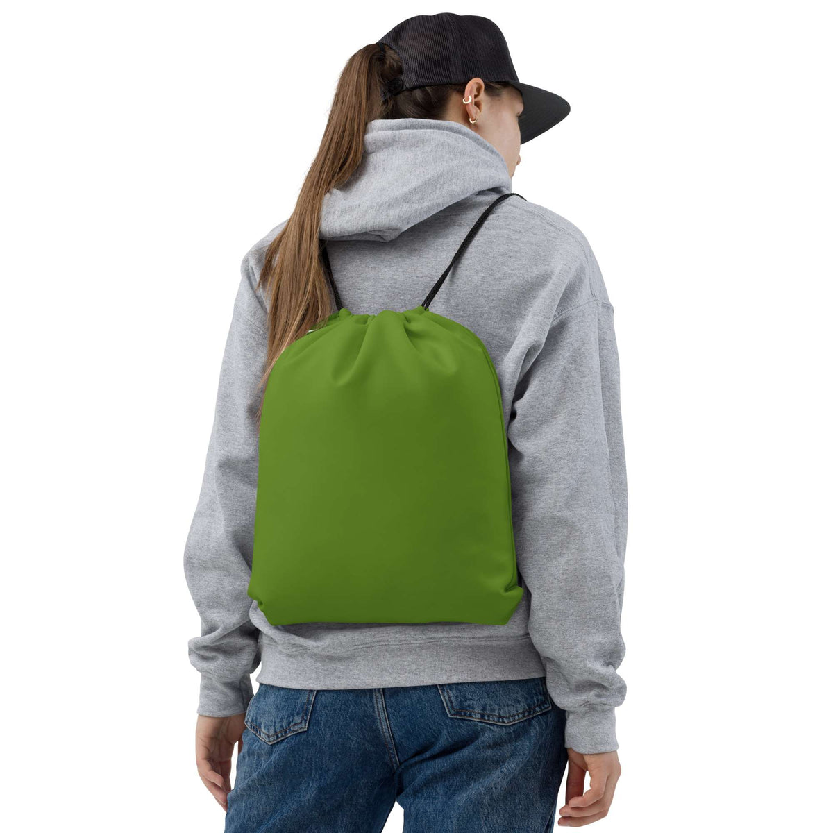 A person viewed from the back wearing a gray hoodie, blue jeans, and a black baseball cap, carrying a bright green drawstring backpack against a plain white background. Essential Minimalist Bold Solid Olive Drab Drawstring Bag
