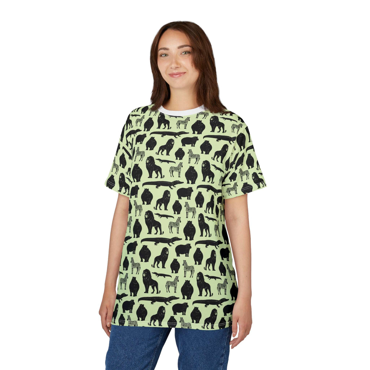 A woman modeling a short-sleeve t-shirt with a repeating black animal silhouette pattern on a light sage green background, paired with blue jeans against a plain white studio background. Vibrant Bold Jungle Safari Animal Pattern T-Shirt for Casual Wear