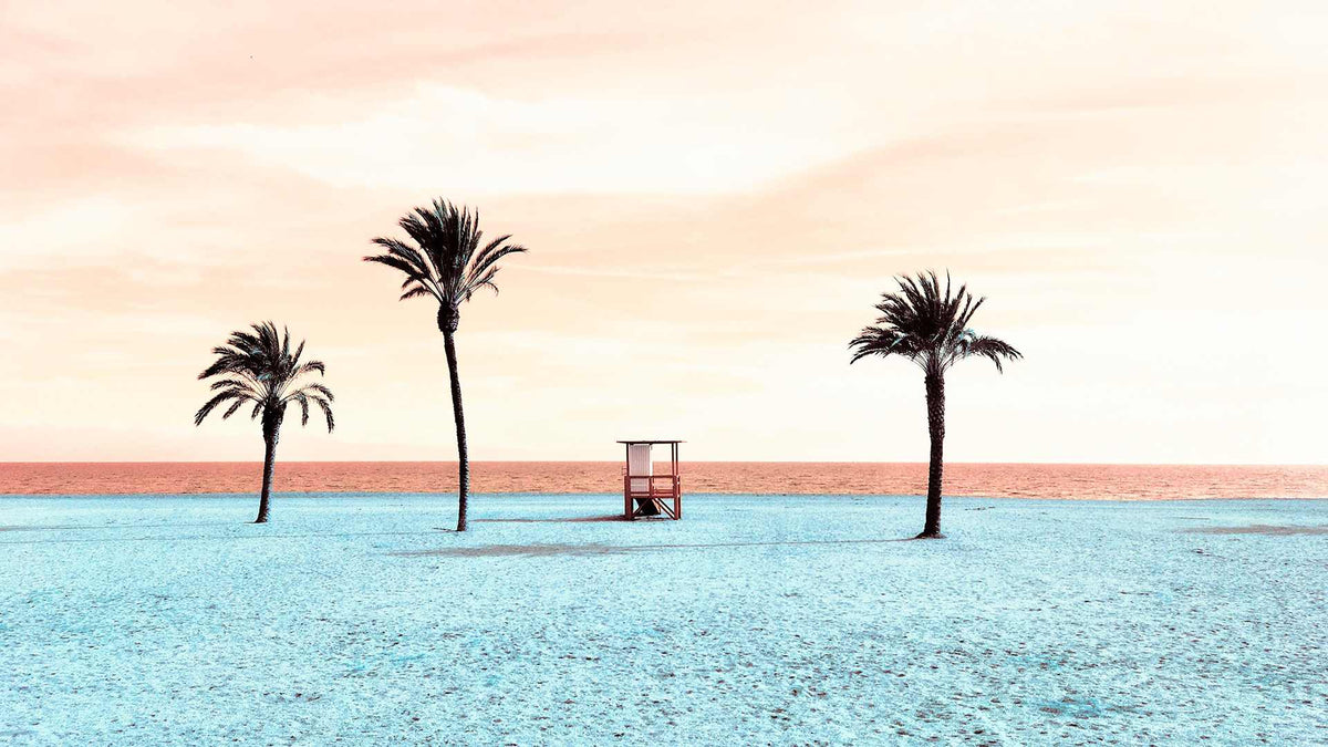 Three palm trees and a lifeguard stand on a beach with clear blue water and a pink sky.
